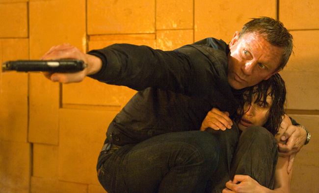 Bond (Daniel Craig) shields Camille (Olga Kurylenko) in Quantum of Solace and fires at a fuel cell as flames engulf Medrano's suite at Perla De Las Dunas