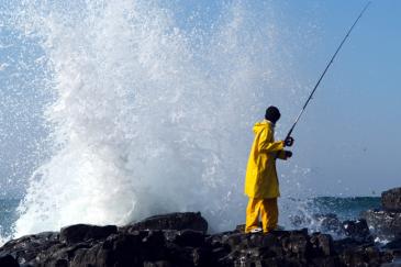 Breaking surf sprays behind a fisherman on the rocks of Sezela Beach, KwaZulu-Natal in the IMAX film Wild Ocean 3-D